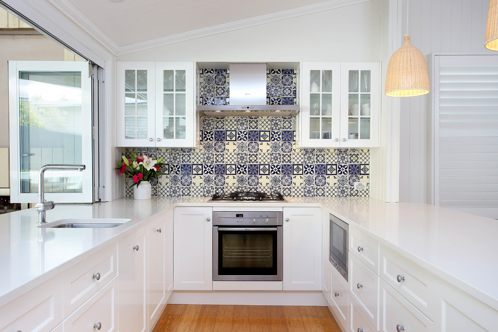 Bild på ett mellanstort funkis vit vitt kök, med en undermonterad diskho, skåp i shakerstil, vita skåp, bänkskiva i kvarts, flerfärgad stänkskydd, stänkskydd i porslinskakel, rostfria vitvaror och ljust trägolv