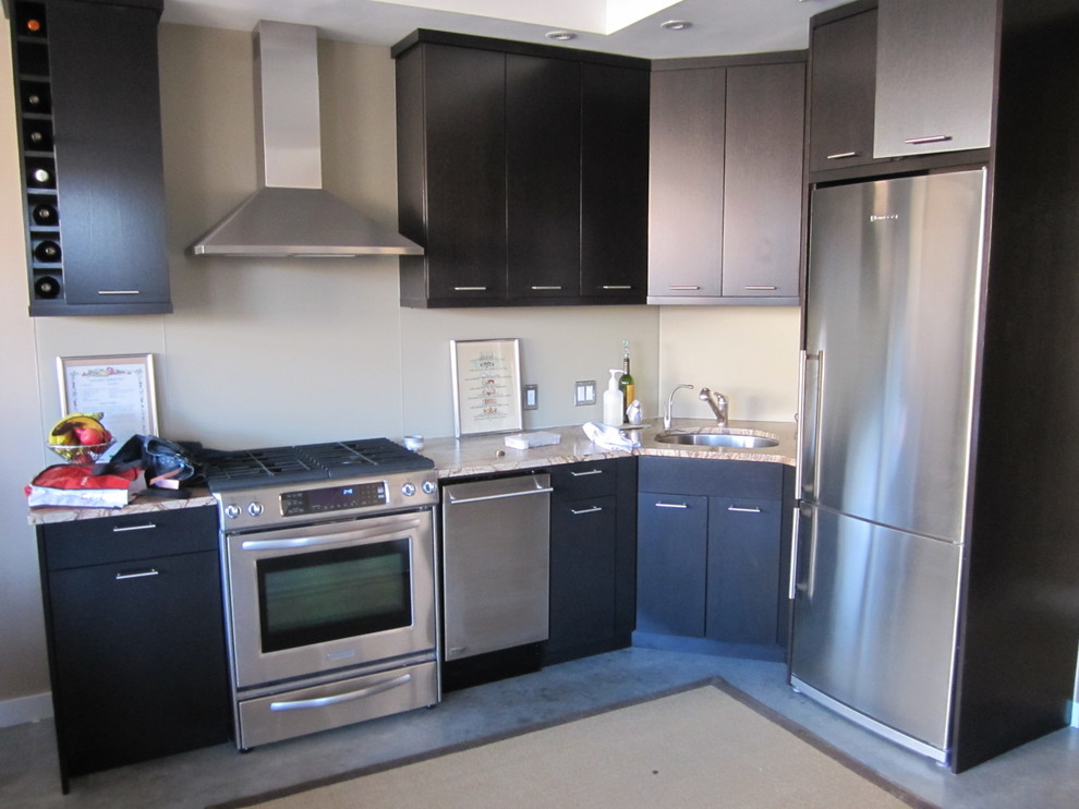 Exempel på ett litet modernt l-kök, med skåp i shakerstil, svarta skåp, granitbänkskiva, rostfria vitvaror, betonggolv, en undermonterad diskho, vitt stänkskydd och glaspanel som stänkskydd