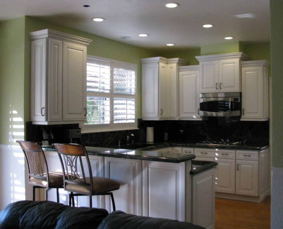 Inredning av ett klassiskt litet u-kök, med vita skåp, granitbänkskiva, svart stänkskydd och rostfria vitvaror