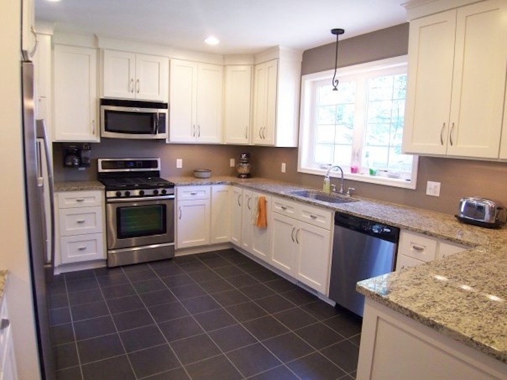 Example of a mid-sized danish u-shaped black floor enclosed kitchen design in Minneapolis with a drop-in sink, raised-panel cabinets, white cabinets, beige backsplash, stainless steel appliances and no island