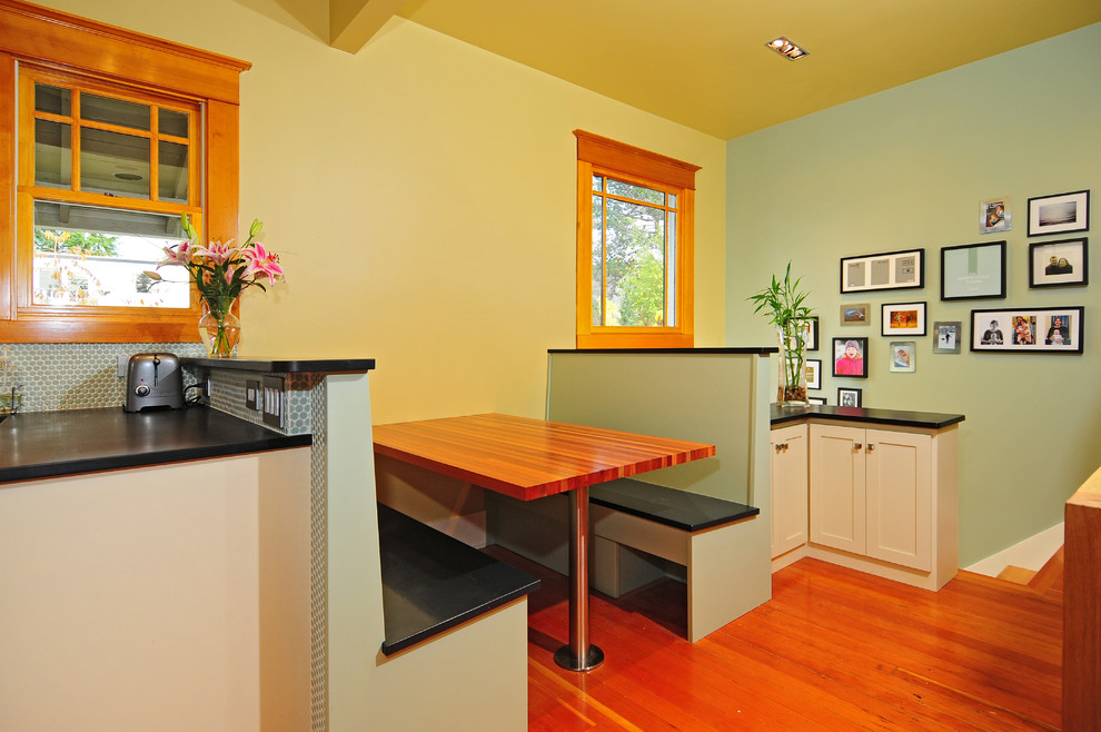 Example of a small transitional u-shaped medium tone wood floor eat-in kitchen design in Seattle with an undermount sink, glass-front cabinets, white cabinets, white backsplash, ceramic backsplash, stainless steel appliances and no island