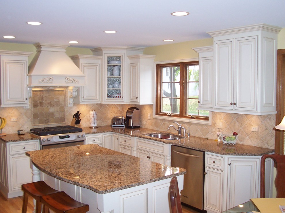 Exemple d'une cuisine américaine chic en L avec des portes de placard blanches, un plan de travail en granite, une crédence beige, parquet clair et îlot.