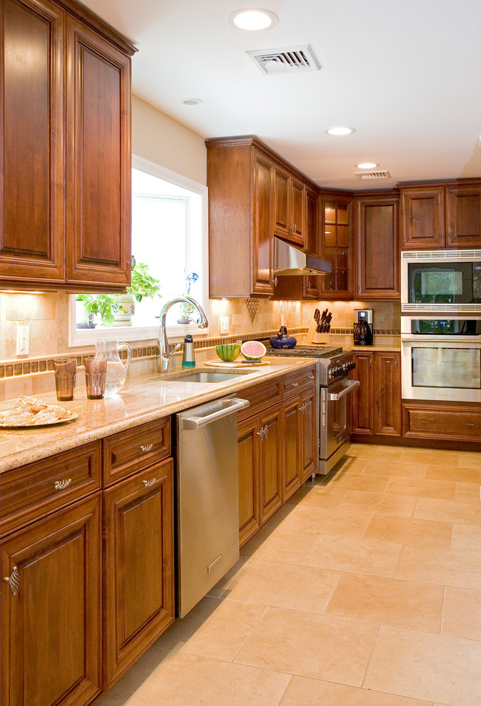 Example of a large transitional ceramic tile kitchen design in New York with an undermount sink, raised-panel cabinets, medium tone wood cabinets, granite countertops, beige backsplash, ceramic backsplash, stainless steel appliances and an island