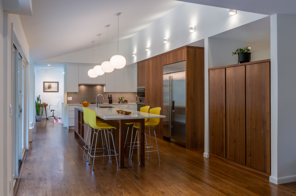 Example of a mid-century modern medium tone wood floor, brown floor and vaulted ceiling eat-in kitchen design in Philadelphia with flat-panel cabinets, medium tone wood cabinets, quartz countertops, gray backsplash, porcelain backsplash, an island, white countertops, an undermount sink and stainless steel appliances