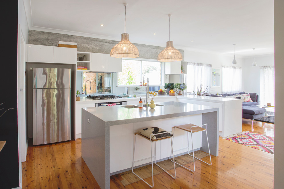 Cette image montre une cuisine design en L avec un placard à porte plane, des portes de placard blanches, un sol en bois brun et îlot.