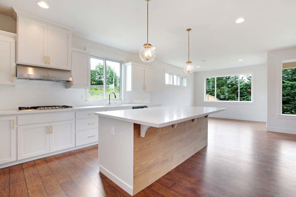 Photo of a medium sized modern l-shaped open plan kitchen in Seattle with a double-bowl sink, shaker cabinets, white cabinets, quartz worktops, white splashback, metro tiled splashback, stainless steel appliances, medium hardwood flooring, an island and brown floors.