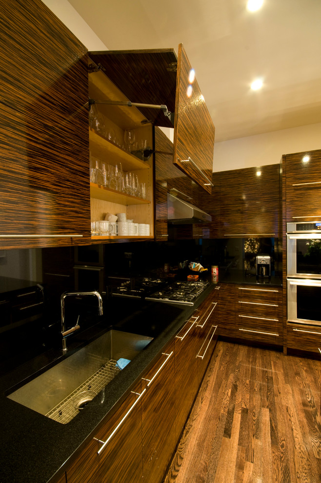 Esempio di una cucina contemporanea di medie dimensioni con lavello sottopiano, ante lisce, ante in legno bruno, top in granito, paraspruzzi nero, elettrodomestici in acciaio inossidabile e pavimento in legno massello medio