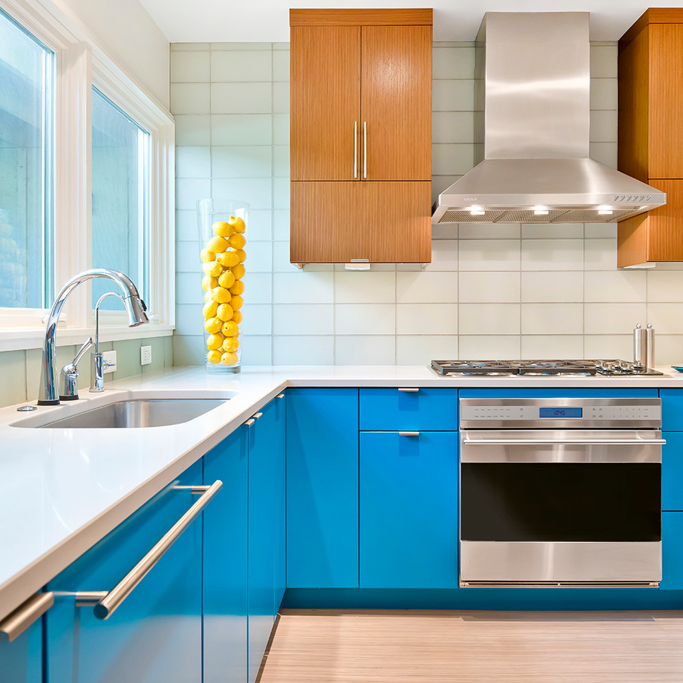 Moderne Küche in L-Form mit Unterbauwaschbecken, flächenbündigen Schrankfronten, blauen Schränken, Küchenrückwand in Weiß, Rückwand aus Glasfliesen, Küchengeräten aus Edelstahl und hellem Holzboden in Chicago