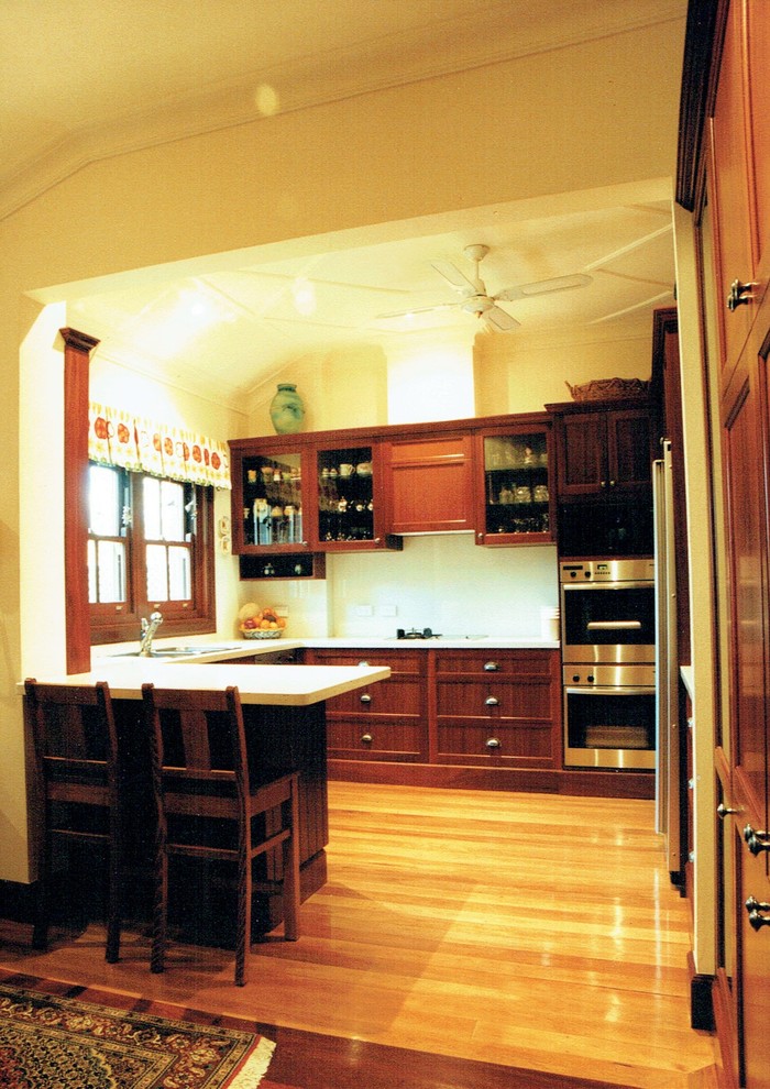 Foto på ett mellanstort vintage kök, med en undermonterad diskho, skåp i mörkt trä, rostfria vitvaror, luckor med infälld panel, bänkskiva i kvarts, vitt stänkskydd, stänkskydd i keramik och ljust trägolv