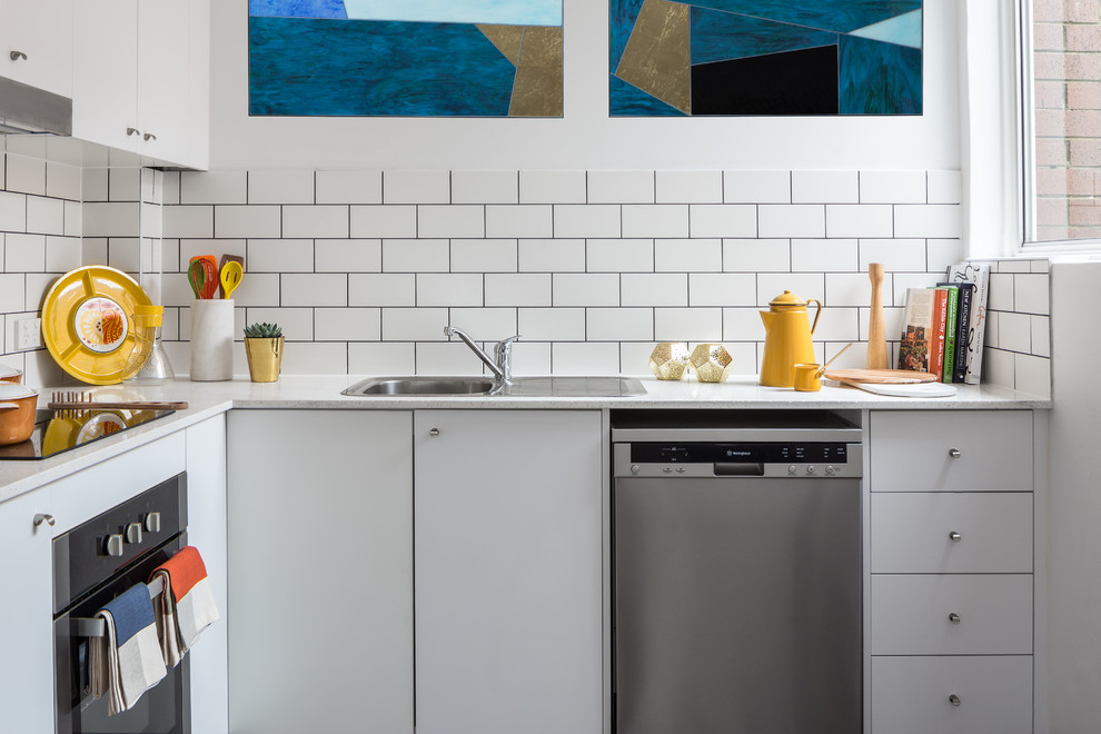 シドニーにあるコンテンポラリースタイルのおしゃれなL型キッチン (ドロップインシンク、フラットパネル扉のキャビネット、白いキャビネット、白いキッチンパネル、サブウェイタイルのキッチンパネル、シルバーの調理設備、アイランドなし) の写真