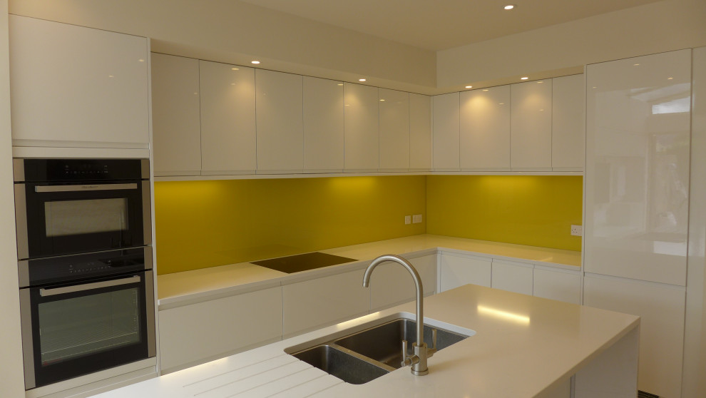 Inspiration for a medium sized contemporary l-shaped open plan kitchen in Other with a submerged sink, flat-panel cabinets, white cabinets, quartz worktops, yellow splashback, glass sheet splashback, stainless steel appliances, porcelain flooring, an island, beige floors, white worktops and a vaulted ceiling.