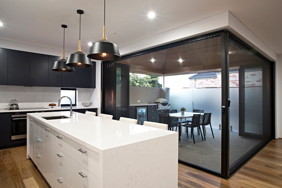 This is an example of a contemporary kitchen in Perth with a submerged sink, black cabinets, composite countertops, white splashback, stone slab splashback, stainless steel appliances, light hardwood flooring and an island.