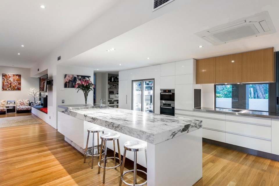 Foto på ett stort funkis kök, med en dubbel diskho, släta luckor, vita skåp, granitbänkskiva, stänkskydd med metallisk yta, stänkskydd i metallkakel, rostfria vitvaror, mellanmörkt trägolv och en köksö