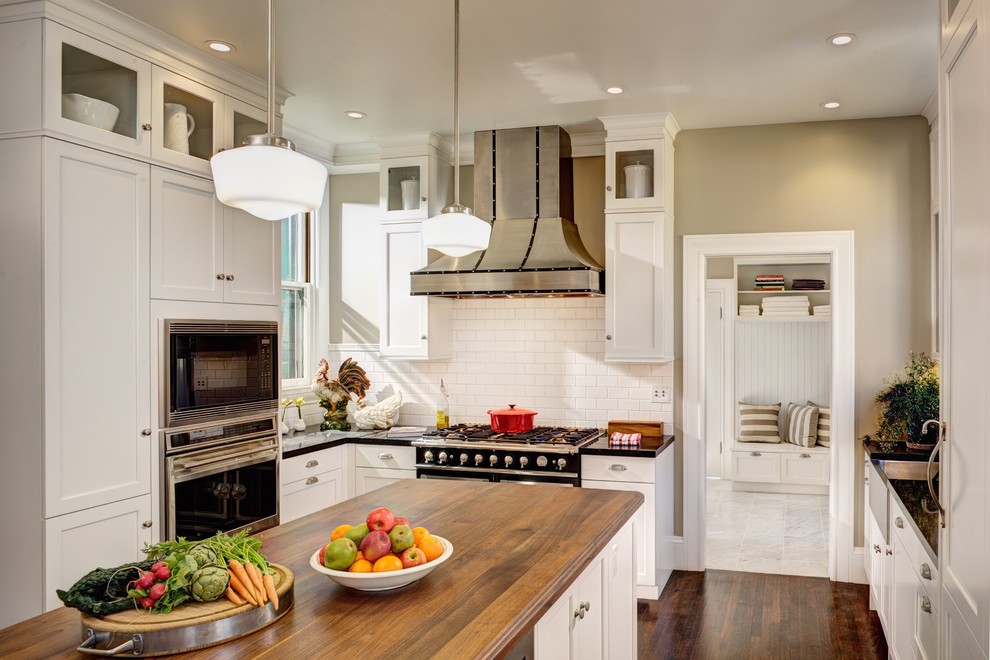 Klassische Küche in L-Form mit weißen Schränken, Küchenrückwand in Weiß, dunklem Holzboden, Kücheninsel und Rückwand aus Metrofliesen in Sacramento
