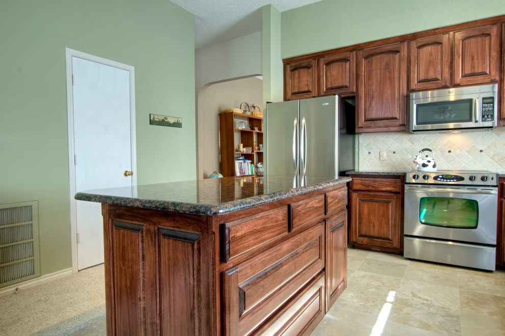 Bild på ett avskilt, mellanstort funkis l-kök, med en undermonterad diskho, luckor med upphöjd panel, skåp i mörkt trä, granitbänkskiva, beige stänkskydd, stänkskydd i keramik, rostfria vitvaror, travertin golv och en köksö