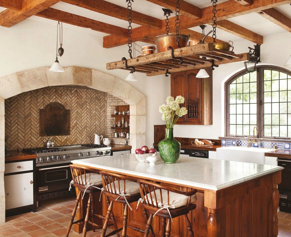 Foto de cocina mediterránea con fregadero sobremueble, salpicadero beige, electrodomésticos negros, suelo de baldosas de terracota, una isla y suelo naranja