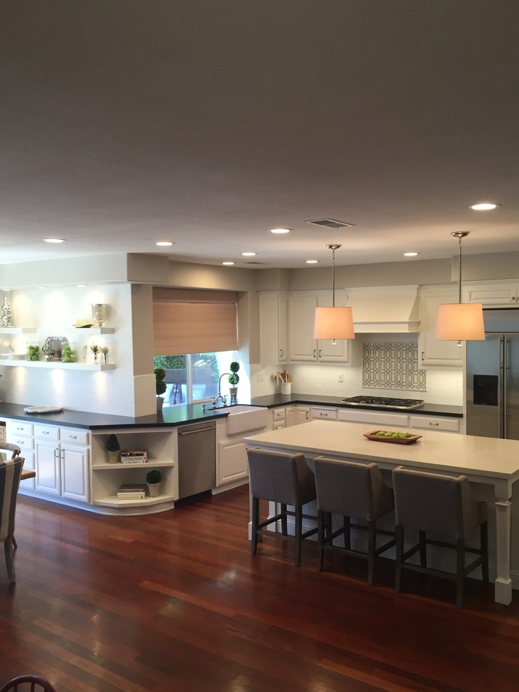 This is an example of a medium sized classic l-shaped enclosed kitchen in San Francisco with a belfast sink, raised-panel cabinets, white cabinets, engineered stone countertops, white splashback, metro tiled splashback, stainless steel appliances, dark hardwood flooring and an island.