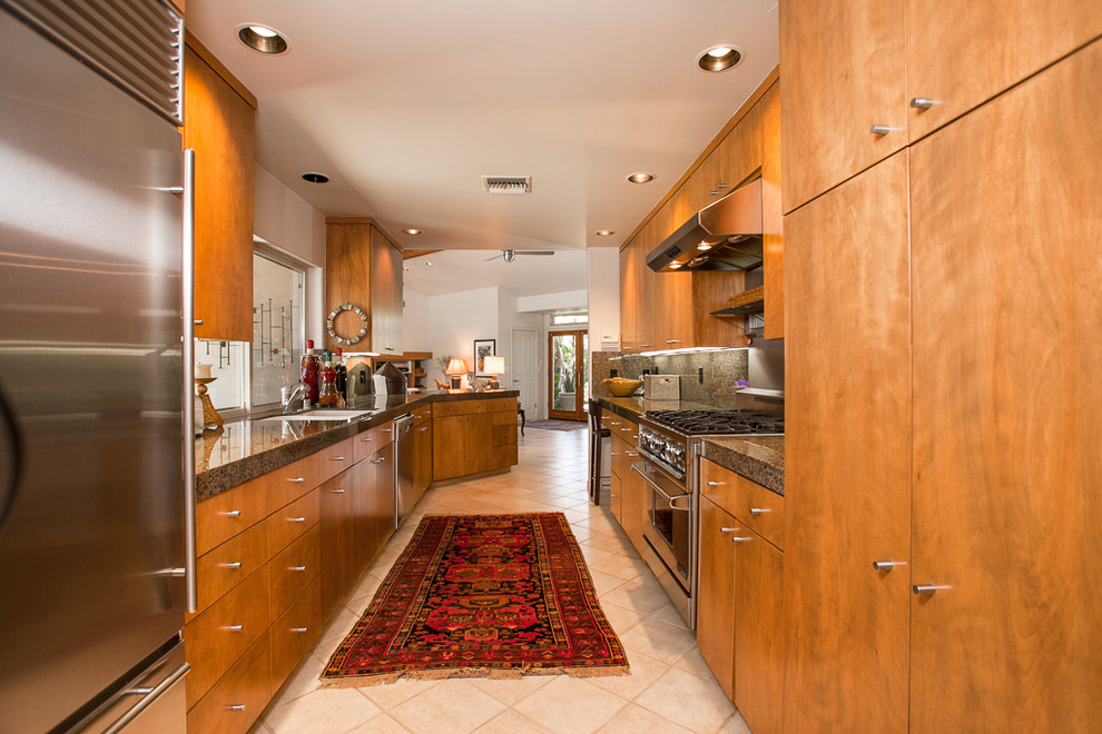 他の地域にあるコンテンポラリースタイルのおしゃれなキッチン (フラットパネル扉のキャビネット、シルバーの調理設備、石スラブのキッチンパネル、中間色木目調キャビネット) の写真