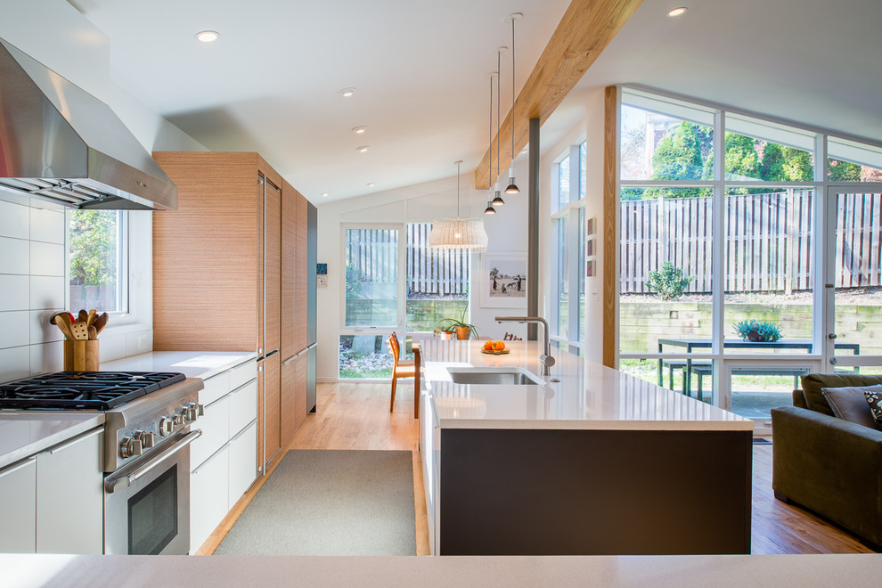 Immagine di una cucina design con lavello sottopiano, ante lisce, ante in legno chiaro, elettrodomestici in acciaio inossidabile e parquet chiaro