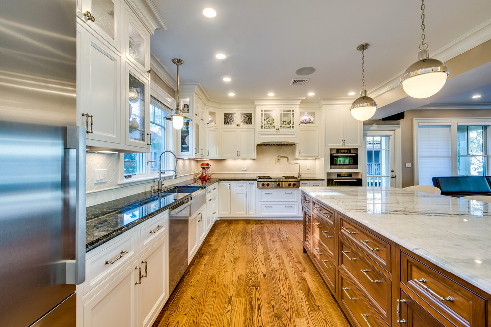 Example of a mid-sized transitional l-shaped medium tone wood floor and brown floor open concept kitchen design in Boston with a farmhouse sink, recessed-panel cabinets, white cabinets, onyx countertops, beige backsplash, ceramic backsplash, stainless steel appliances and an island