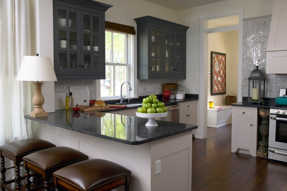 Amerikansk inredning av ett kök, med en undermonterad diskho, luckor med profilerade fronter, vita skåp, granitbänkskiva, grått stänkskydd, stänkskydd i mosaik och rostfria vitvaror