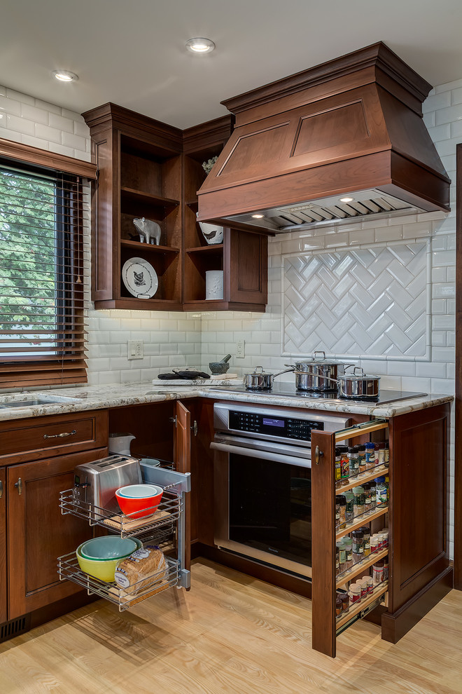 Photo of a traditional kitchen in Calgary with recessed-panel cabinets, dark wood cabinets, white splashback, metro tiled splashback, stainless steel appliances and light hardwood flooring.