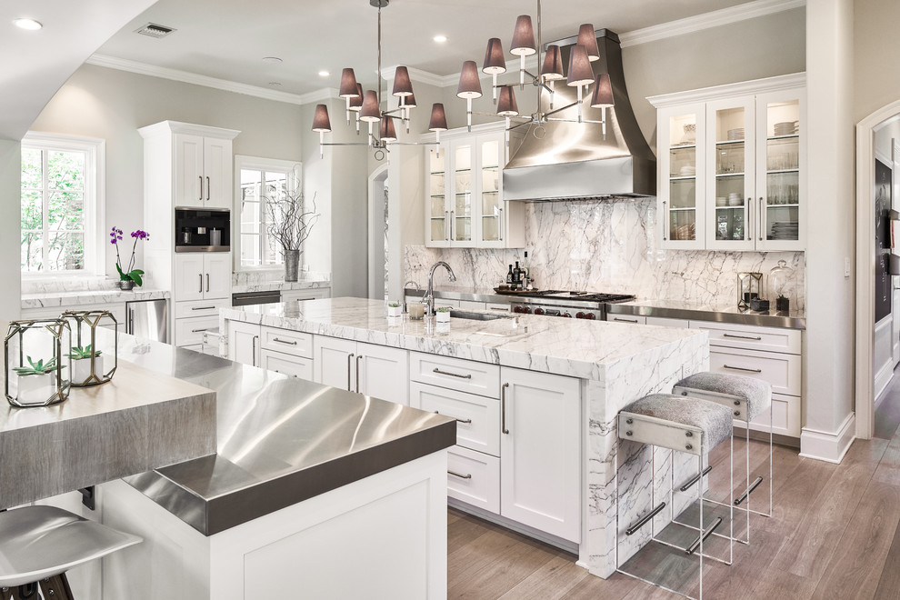 Inspiration for a traditional u-shaped kitchen in Austin with glass-front cabinets, white cabinets, marble worktops, stainless steel appliances, multiple islands, white splashback, stone slab splashback and medium hardwood flooring.