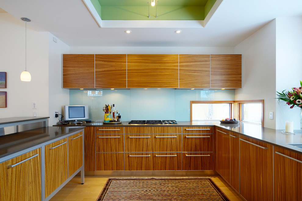 Imagen de cocina actual con armarios con paneles lisos, puertas de armario de madera oscura, salpicadero azul y salpicadero de vidrio templado