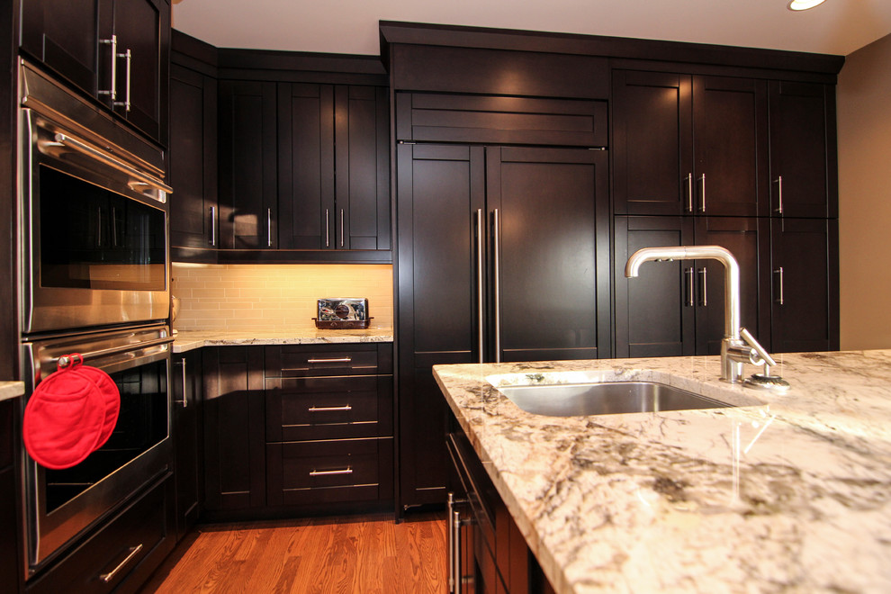 This is an example of a large traditional u-shaped kitchen/diner in Calgary with a submerged sink, recessed-panel cabinets, black cabinets, granite worktops, beige splashback, matchstick tiled splashback, stainless steel appliances, dark hardwood flooring, an island, brown floors and beige worktops.