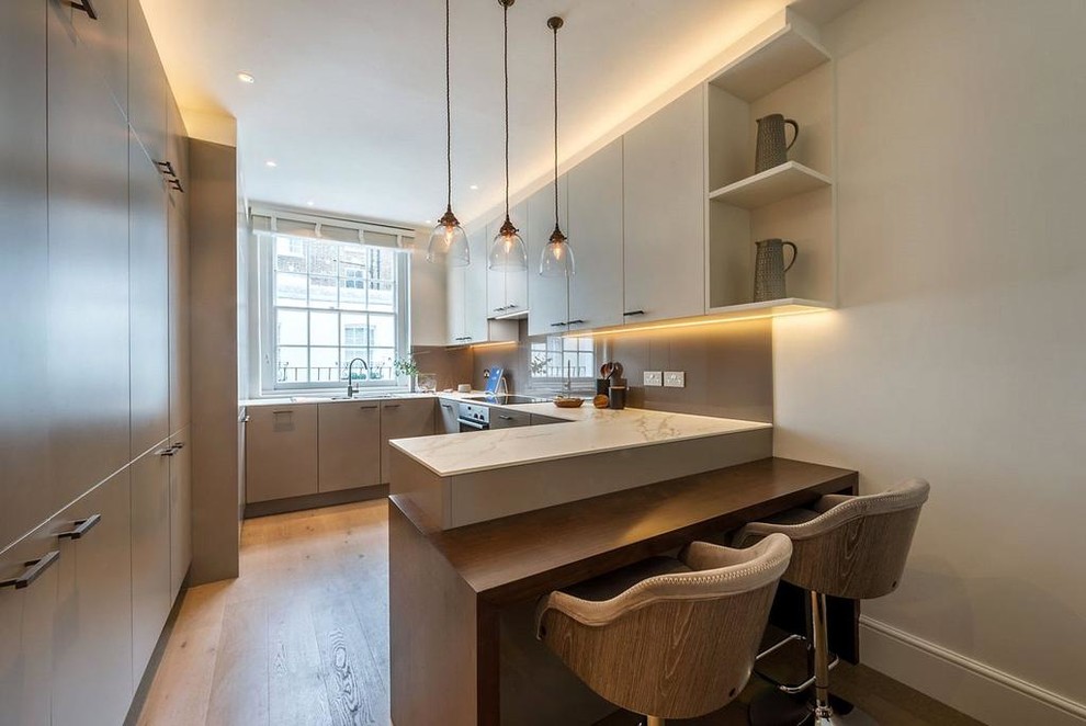 Example of a mid-sized trendy u-shaped light wood floor and beige floor kitchen design in London with flat-panel cabinets, gray cabinets, marble countertops, a peninsula, white countertops, gray backsplash and glass sheet backsplash
