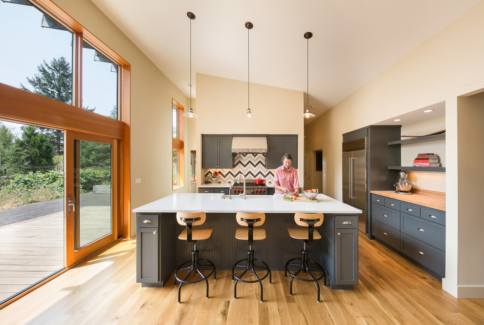 Bild på ett lantligt kök med öppen planlösning, med en rustik diskho, skåp i shakerstil, grå skåp, bänkskiva i kvarts, flerfärgad stänkskydd, stänkskydd i keramik, rostfria vitvaror, ljust trägolv och en köksö