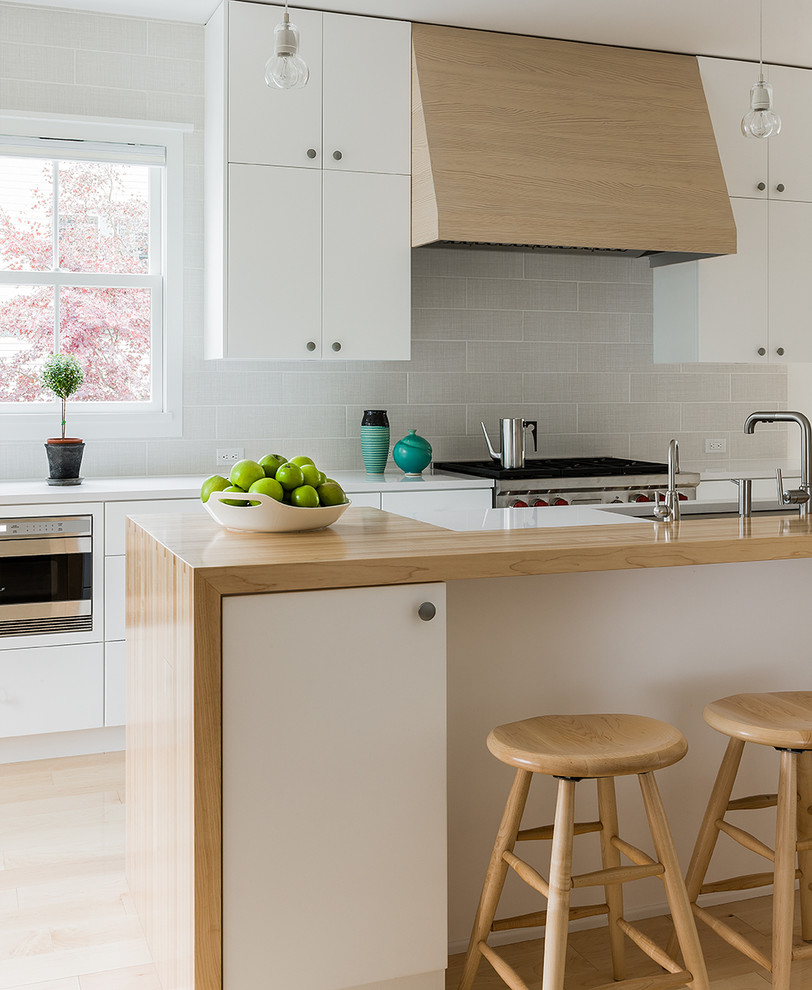 Photo of a contemporary kitchen in Boston with a submerged sink, flat-panel cabinets, white cabinets, wood worktops, grey splashback, metro tiled splashback, stainless steel appliances, light hardwood flooring and an island.