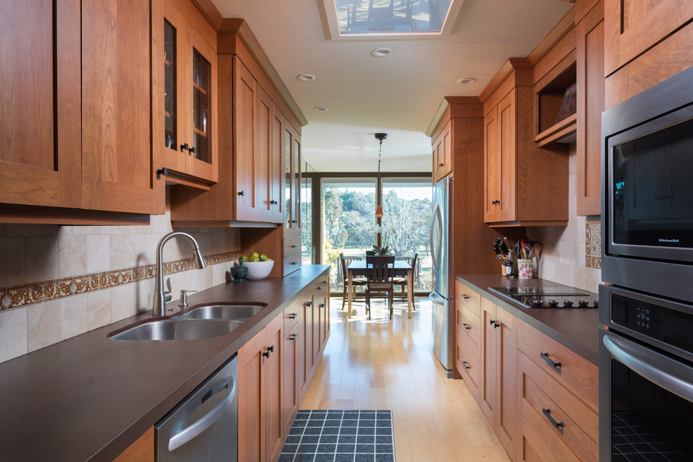 Cette image montre une cuisine américaine parallèle traditionnelle en bois brun avec un évier 2 bacs, un placard à porte shaker, une crédence multicolore, parquet clair, aucun îlot, un sol beige et un plan de travail marron.