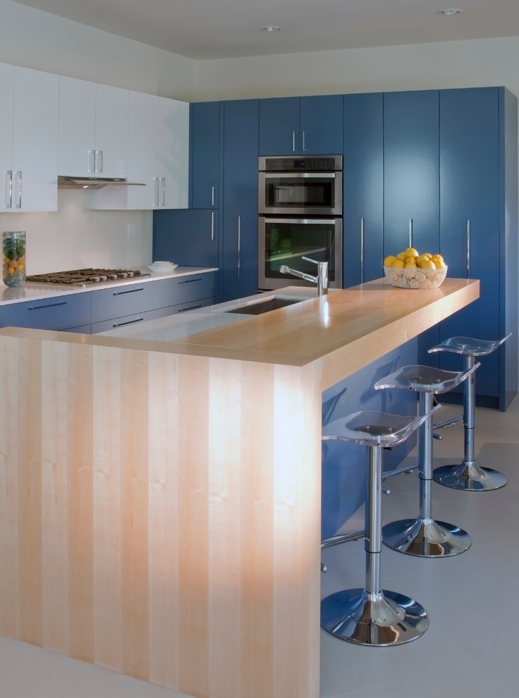 Exempel på ett modernt l-kök, med stänkskydd i sten, rostfria vitvaror, en undermonterad diskho, släta luckor, blå skåp, bänkskiva i kvarts, vitt stänkskydd, klinkergolv i porslin och en köksö