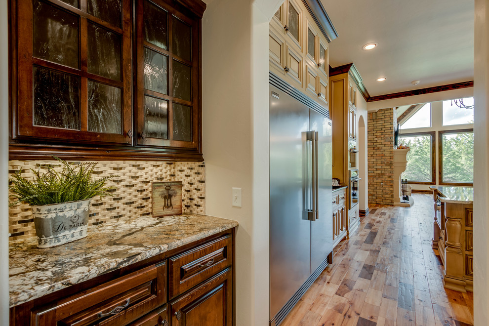 Klassische Wohnküche mit Granit-Arbeitsplatte, Küchenrückwand in Beige, Rückwand aus Steinfliesen, Küchengeräten aus Edelstahl, hellem Holzboden und Kücheninsel in Oklahoma City