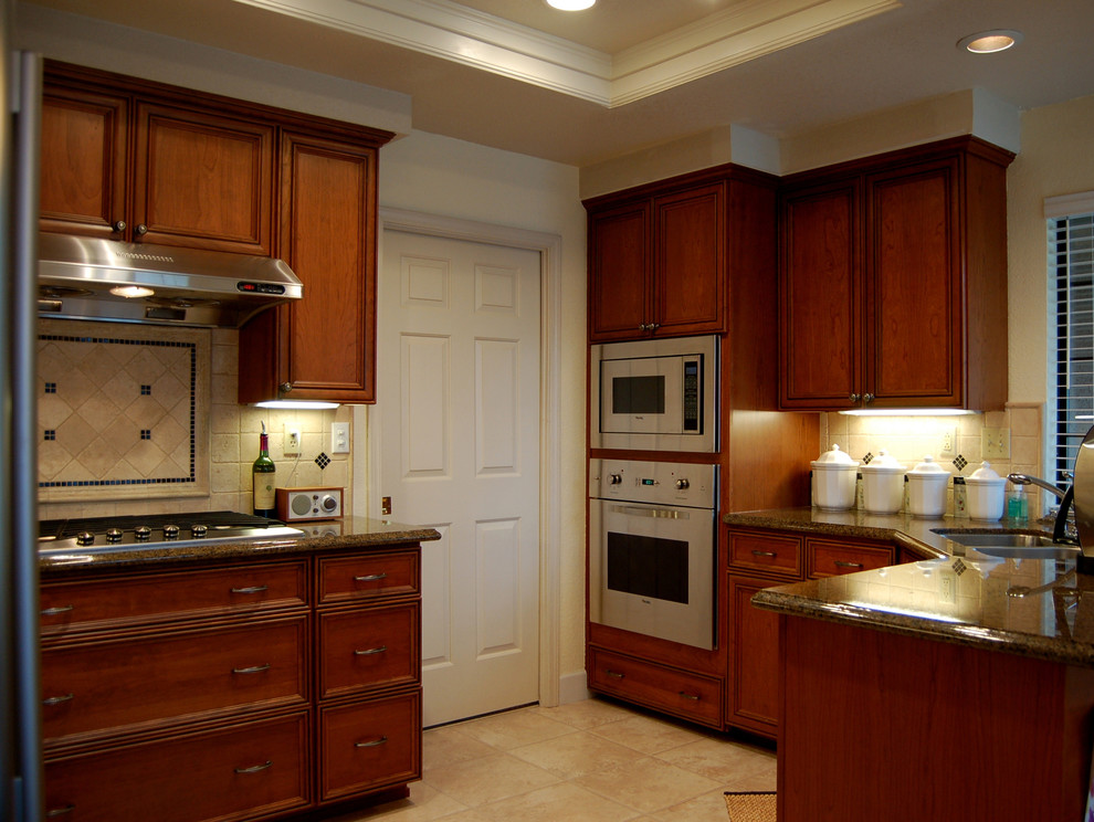 Inredning av ett klassiskt kök, med en dubbel diskho, luckor med upphöjd panel, skåp i mellenmörkt trä, rostfria vitvaror, klinkergolv i keramik och en halv köksö