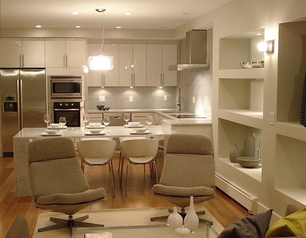 На фото: п-образная кухня-гостиная в современном стиле с техникой из нержавеющей стали, плоскими фасадами, белыми фасадами и серым фартуком с