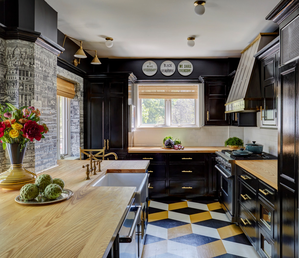 Inspiration for a timeless l-shaped painted wood floor and multicolored floor kitchen remodel in Chicago with a farmhouse sink, shaker cabinets, black cabinets, wood countertops, white backsplash, subway tile backsplash, stainless steel appliances, no island and brown countertops