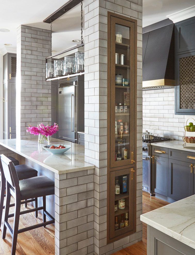 Cette image montre une cuisine traditionnelle avec un placard à porte shaker, des portes de placard bleues, une crédence grise, une crédence en carrelage métro, un électroménager en acier inoxydable et un sol en bois brun.
