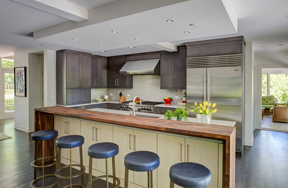 Example of a trendy l-shaped dark wood floor kitchen design in Chicago with an undermount sink, flat-panel cabinets, brown cabinets, white backsplash, glass sheet backsplash, stainless steel appliances and an island