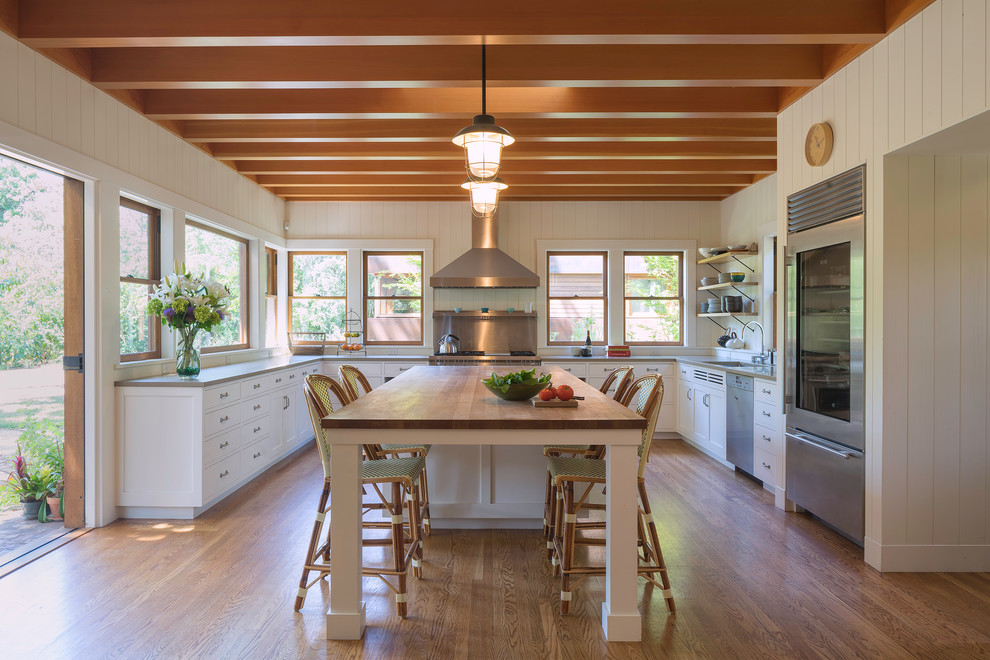 Immagine di una cucina classica con ante in stile shaker, ante bianche, elettrodomestici in acciaio inossidabile e pavimento in legno massello medio