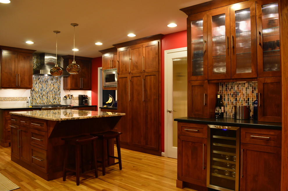 Cette photo montre une cuisine américaine tendance avec un évier encastré, un placard à porte shaker, des portes de placard marrons, un plan de travail en granite, une crédence multicolore et un électroménager en acier inoxydable.