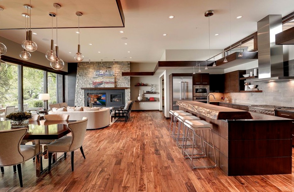 Inredning av ett modernt kök med öppen planlösning, med en undermonterad diskho, bruna skåp, träbänkskiva, grått stänkskydd, stänkskydd i stenkakel, rostfria vitvaror, mellanmörkt trägolv och en köksö