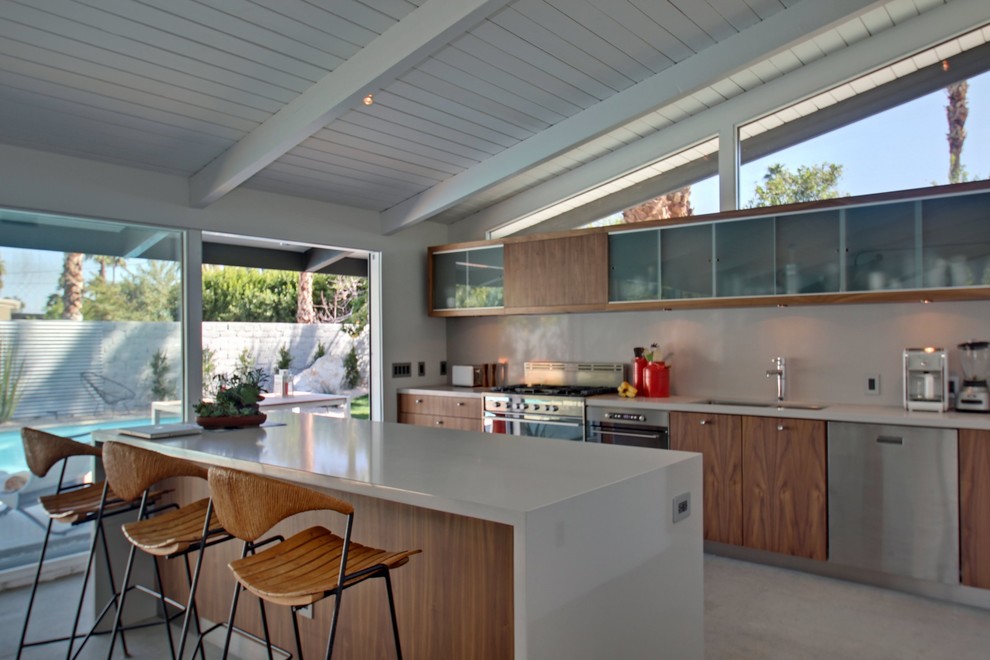 Example of a mid-sized trendy single-wall concrete floor eat-in kitchen design in Los Angeles with a double-bowl sink, flat-panel cabinets, medium tone wood cabinets, white backsplash, stainless steel appliances and an island