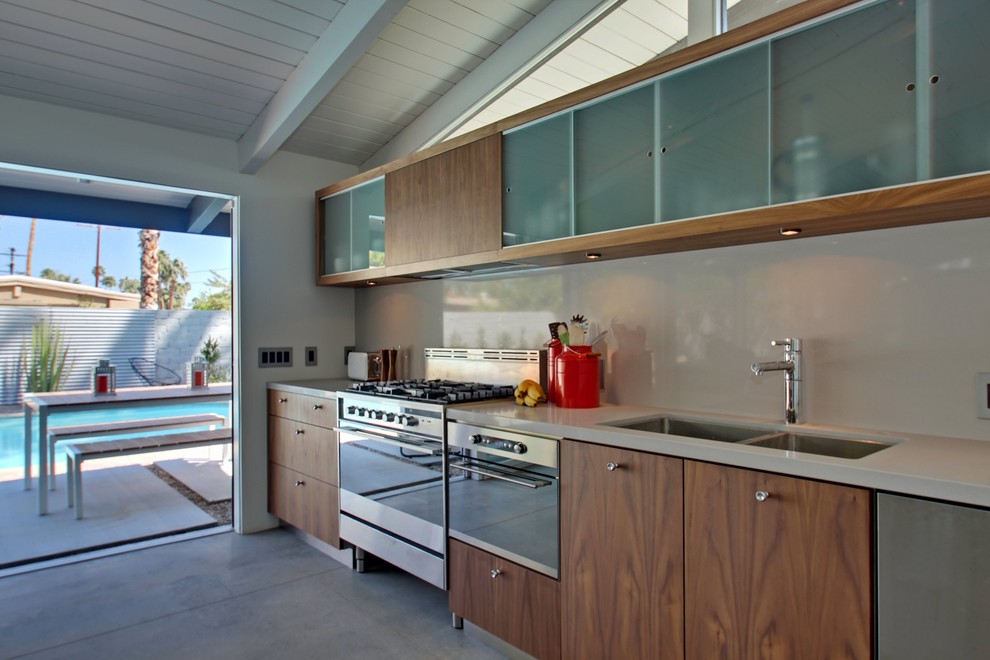 Eat-in kitchen - mid-sized contemporary single-wall concrete floor eat-in kitchen idea in Los Angeles with a double-bowl sink, flat-panel cabinets, medium tone wood cabinets, white backsplash, stainless steel appliances and an island