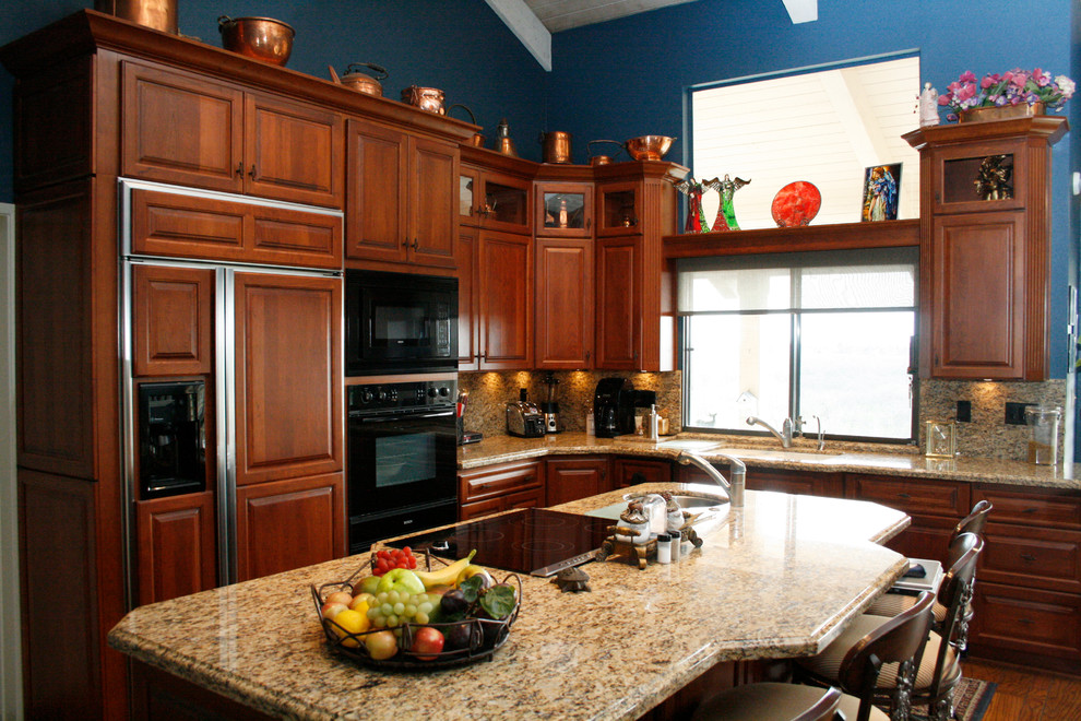 Eat-in kitchen - mid-sized traditional l-shaped medium tone wood floor eat-in kitchen idea in Sacramento with a double-bowl sink, raised-panel cabinets, medium tone wood cabinets, granite countertops, stone slab backsplash, black appliances and an island