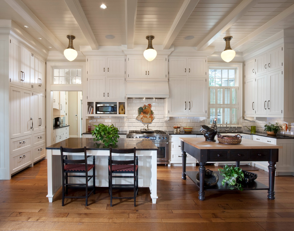 Design ideas for a farmhouse kitchen in Milwaukee with a belfast sink, recessed-panel cabinets, white cabinets, white splashback, stainless steel appliances, medium hardwood flooring and multiple islands.