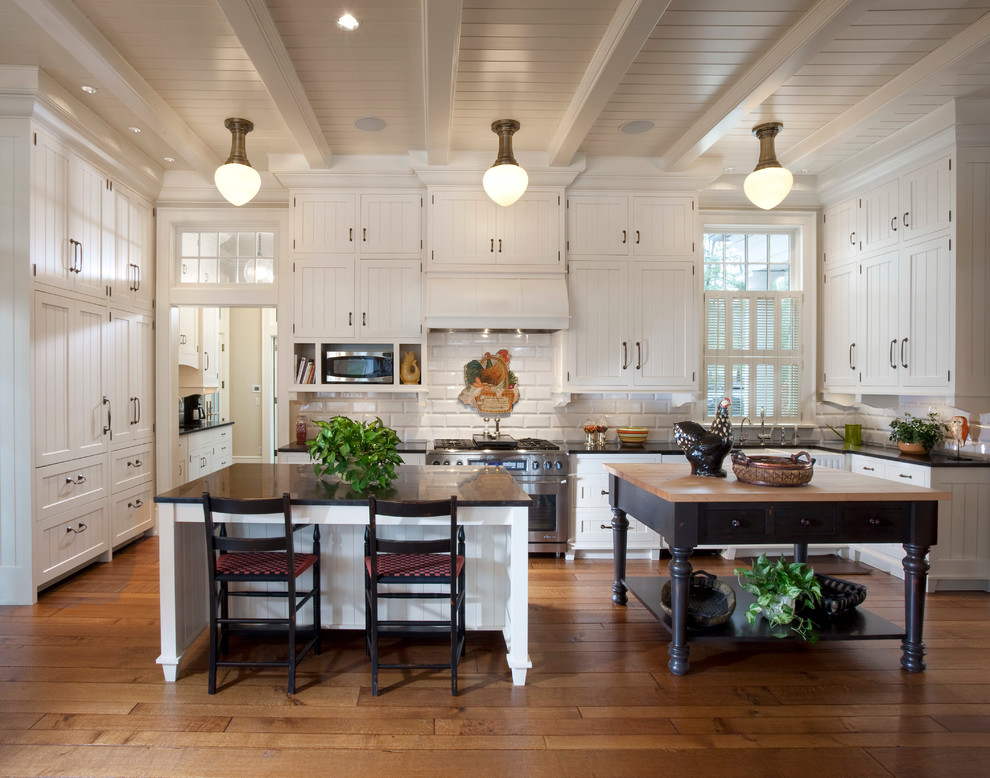 Country medium tone wood floor kitchen photo in Milwaukee with a farmhouse sink, recessed-panel cabinets, white cabinets, white backsplash, stainless steel appliances and two islands