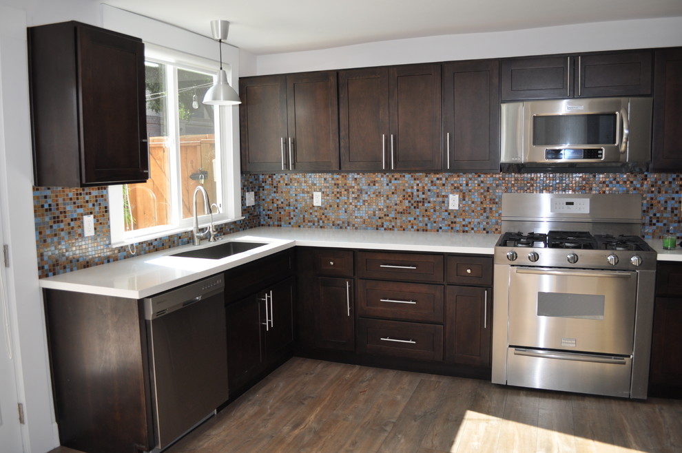 Example of a l-shaped open concept kitchen design in San Francisco with beaded inset cabinets, dark wood cabinets, metallic backsplash, glass tile backsplash, stainless steel appliances and no island