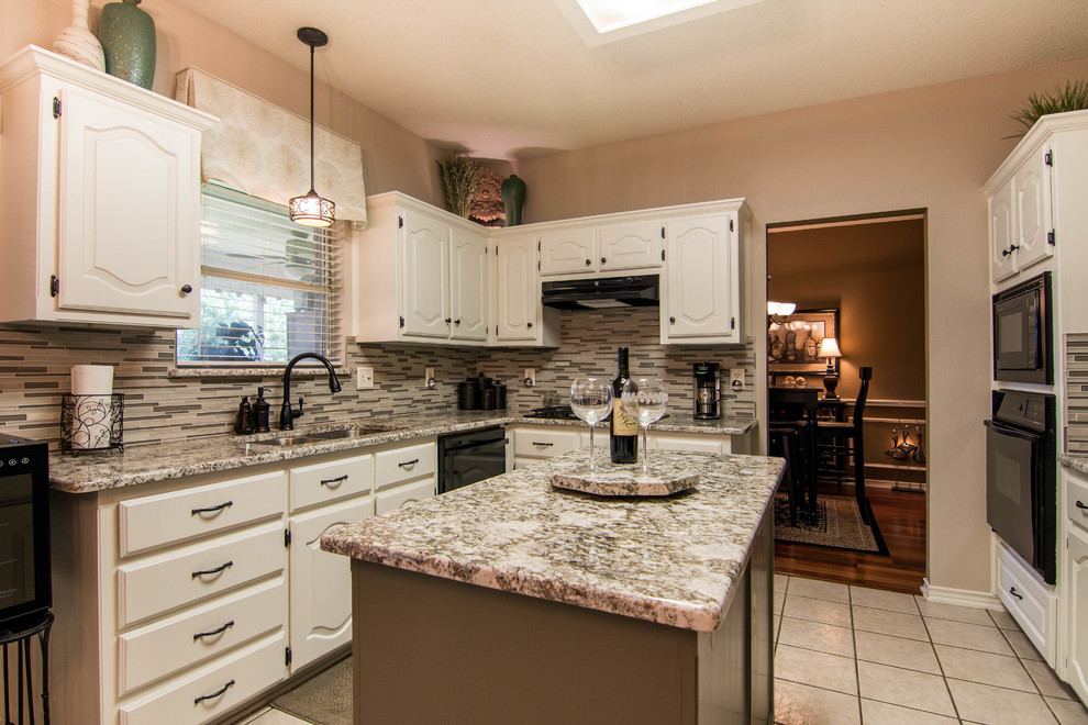 Example of a mid-sized transitional l-shaped ceramic tile and white floor enclosed kitchen design in Dallas with a double-bowl sink, raised-panel cabinets, white cabinets, granite countertops, multicolored backsplash, glass tile backsplash, black appliances and an island